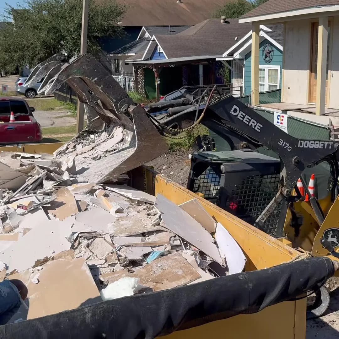 Track loader with a grapple dropping demolition debris into a Bolt dump trailer