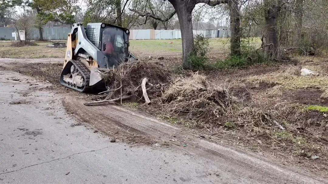 Track loader grappling brush along a cleared roadside